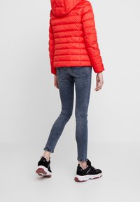 Rød dunjakke med hætte, quiltet tekstur, tætsiddende silhuet. Båret med mørkeblå jeans og sorte sneakers med hvide såler.