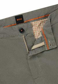 Pantaloni grigi a fantasia con etichetta BOSS. Caratterizzati da un bottone e una zip in metallo, dettagli arancioni a contrasto e fodera interna beige.