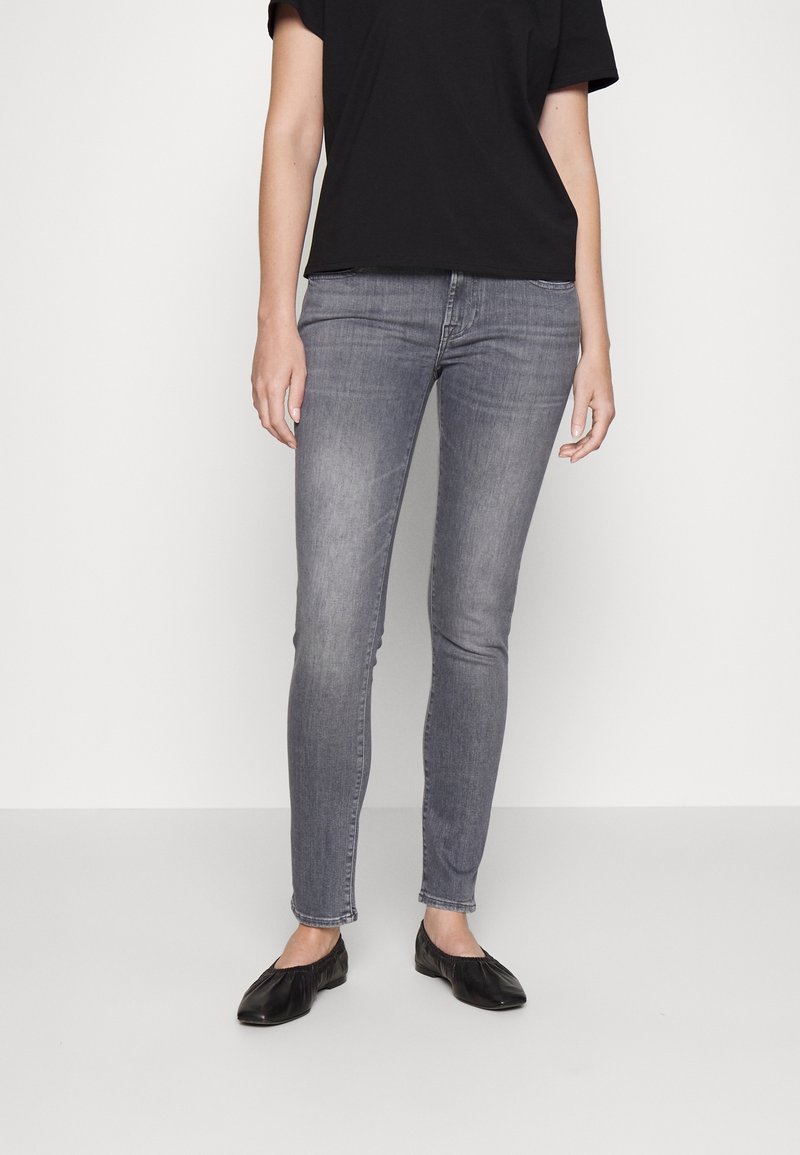 Jean skinny en denim gris associé à une chemise noire à manches courtes et des ballerines noires. Le jean présente une texture lisse avec une coupe ajustée.
