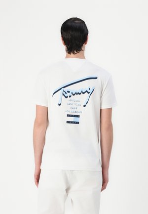 Hvid bomulds t-shirt med et blåt og marineblåt grafisk logo på ryggen, der viser bynavne og brandnavn i forskellige skrifttyper.