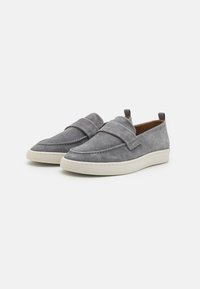 Chaussures en suède gris à enfiler avec une bande supérieure rembourrée et une semelle en caoutchouc blanc. Texture lisse avec des détails cousus. Design minimaliste, sans matériel visible.