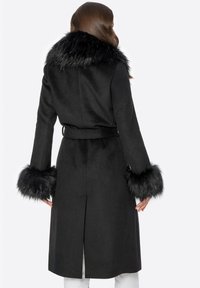Schwarzer Mantel mit einem Kragen und Manschetten aus Kunstpelz. Besitzt eine taillierte Taille, lange Ärmel und eine leicht ausgestellte Silhouette. Glatte Textur.