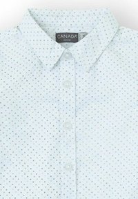 Camisa blanca de botones con pequeños lunares azules y marrones y un cuello puntiagudo, etiquetada "CANADÁ" en el interior del escote.