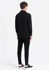 Musta pitkähiha polo, jossa on kaulus, yhdistettynä mustiin housuihin ja mustiin lenkkikenkiin valkoisilla yksityiskohdilla, esittäen muotoiltua suunnittelua ja sileää kangasta.