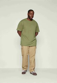 Πράσινο-ελαιί χρώμα βαμβακερό t-shirt με κοντά μανίκια, συνδυασμένο με χακί cargo παντελόνια. Το t-shirt έχει ένα μικρό λογότυπο, τα παντελόνια διαθέτουν πλαϊνές τσέπες.