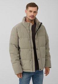 Gepolsterte Jacke aus hellgrauem Cord mit Stehkragen, Druckknöpfen und zwei vorderen Taschen; getragen über einem gestreiften Hemd.
