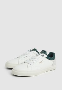 Baskets blanches avec des accents verts et gris, en matériau synthétique lisse, design basse, lacets plats et semelle en caoutchouc texturé.