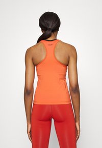 Top deportivo naranja con diseño de espalda nadadora y ribete negro, hecho de material elástico, combinado con leggings rojos ajustados.