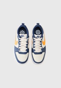 Baskets Nike avec une coque blanche, un corps bleu marine et un swoosh orange. Présente des lacets plats, des détails perforés et le logo sur la languette.