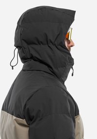 Puffige Kapuzenjacke in Schwarz mit beigen Akzenten. Verfügt über verstellbare Kordeln an der Kapuze und eine glatte, matte Textur.