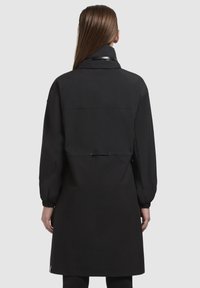 Cappotto lungo nero con colletto, polsini elastici e vita con cordoncino. Tessuto liscio con un design semplice e senza motivi visibili.