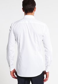 Witte langarm blouse met een klassieke kraag, voorzien van een gladde textuur, een afgeronde zoom en manchetten met knopen, gezien vanaf de achterkant.