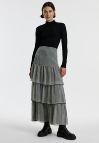 Zwarte geribbelde coltrui gecombineerd met een gelaagde, enkellange rok in een zwart-wit geblokt patroon. Chunky zwarte enkellaarzen maken de look compleet.