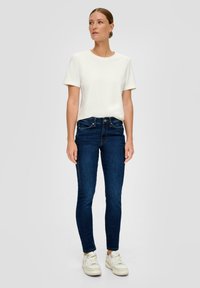 Camiseta de algodón blanca de manga corta, combinada con unos pantalones ajustados azul marino y zapatillas blancas. Diseño simple, sin patrones ni elementos destacados.