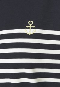 Námořnická a bílá pruhovaná látka má malý žlutě vyšitý symbol kotvy, který zdůrazňuje texturu a kontrastní barvy.