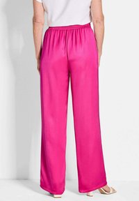 Wijd-vallende broek in felroze satijn, met een elastische tailleband en een gladde textuur. Subtiele glans voegt visuele interesse toe.