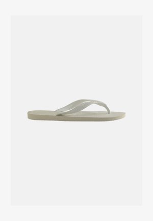 Enkele lichtbeige rubberen teenslipper met een getextureerd voetbed en Y-vormige band op een effen grijze achtergrond.