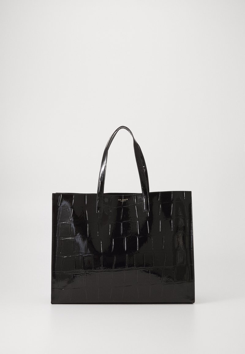 Sac cabas noir brillant avec texture crocodile et deux poignées, debout sur un fond clair uni.