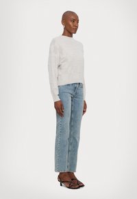 Maglione grigio chiaro con motivo a quadri testurizzati, abbinato a jeans a gamba dritta blu chiaro e tacchi neri con cinturini. Tessuto morbido, design minimale.