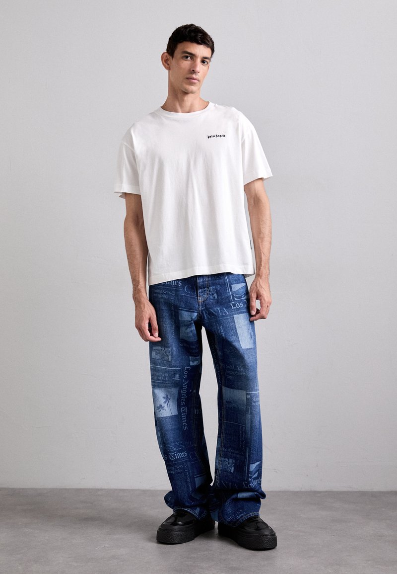 Valge puuvillane T-särk musta tekstiga, millega on koos sinised denim teksad, millel on mustrid ajalehepaberist. Mustad tükilised kingad täiustavad välimust.