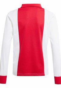 Červeno-biely polo tričko s dlhým rukávom a golierom. Obsahuje kontrastné paneli a rebrované manžety. Vyrobené z hladkej, priedušnej tkaniny.