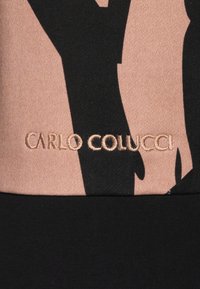 Zwarte en perzikkleurige stof met abstracte vormen. Beige stiksel toont het logo "CARLO COLUCCI". Gladde textuur, strak gebreid ontwerp.