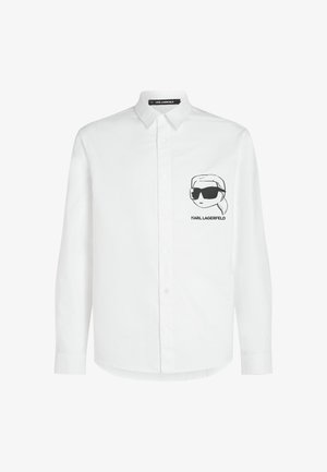 Valge puuvillasegust nööbitav särk, millel on vasakul rinnal must tikand, millel on prillidega karakter.