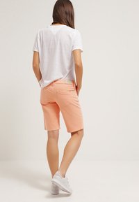 Pantalones cortos ligeros de durazno pastel, hechos de una mezcla de algodón, con un corte clásico, una textura suave y bolsillos traseros, combinados con una camiseta blanca.