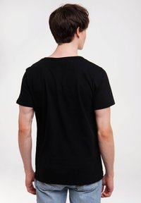 Černé bavlněné tričko s krátkým rukávem a kulatým výstřihem, s volným střihem a hladkým povrchem. Nosené s světle modrými džíny.