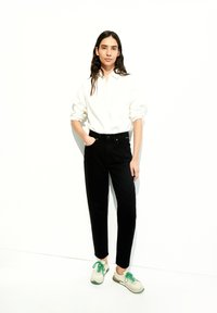 Jeans negros de cintura alta y una camisa blanca de botones, combinados con zapatillas beige con cordones y detalles verdes. Diseño sencillo y colores sólidos.