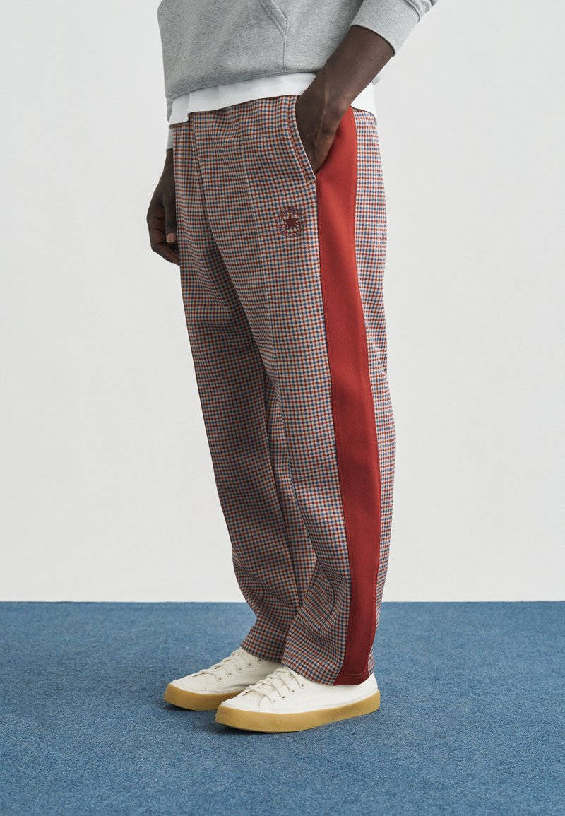 Καρό παντελόνια με κόκκινη ρίγα στο πλάι, κατασκευασμένα από απαλό ύφασμα. Το παντελόνι έχει ελαστική μέση και διακριτική λεπτομέρεια λογότυπου.
