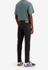 Svarta denimjeans med slim fit, matchade med en teal t-shirt. Vita och marinblå sneakers med bruna sulor fulländar outfiten.