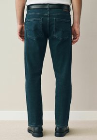 Jeans de mezclilla azul oscuro con corte recto, que cuentan con dos bolsillos traseros y detalles de costura mínimos. Se llevan con un cinturón negro y zapatos negros.