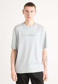 Gray cotton t-shirt with short sleeves and a crew neckline. Features embossed "Calvin Klein" logo on the chest. Straight-cut design.