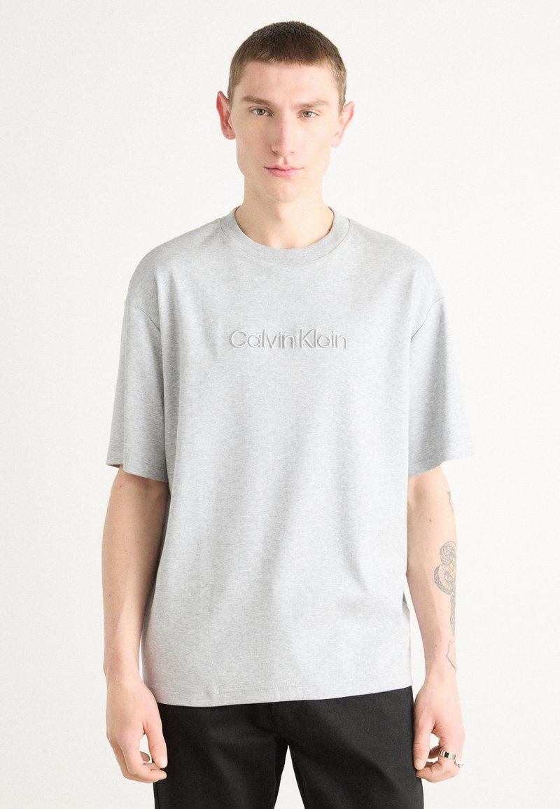 Gray cotton t-shirt with short sleeves and a crew neckline. Features embossed "Calvin Klein" logo on the chest. Straight-cut design.