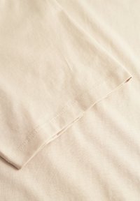 Lys beige stof med en glat tekstur, der har en kantet kant og synlige sømme. Materialet er blødt og lidt strækbart.