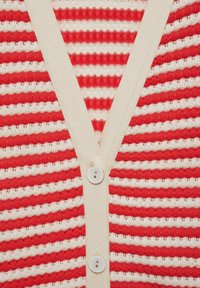 Cardigan a righe rosse e bianche con scollatura a V, tessuto a maglia texturizzato e due bottoni bianchi sul davanti. Accentuato da un colletto color crema.