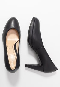 Černé kožené dámské lodičky na vysokém podpatku, jedny viděné z vrchu a druhé z boku, na bílém pozadí.