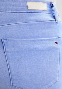 Jeans de mezclilla azul claro con una vista cercana de un bolsillo trasero, que presenta un parche blanco y un pequeño logo en rojo, blanco y azul.