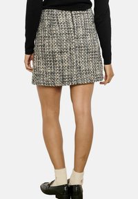 Tweedová mini sukňa v čiernej a krémovej farbe, s textúrovanou látkou, rovný strih a skrytý zips na zadnej strane. Plochý pásový detail.