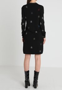 Abito nero lavorato a maglia con maniche lunghe, decorato con motivi stellati multicolori. Presenta un colletto tondo e arriva sopra il ginocchio.