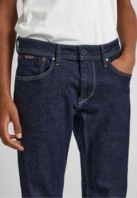 Vaqueros de denim de un azul oscuro con pierna recta, costuras visibles, cinco bolsillos y una etiqueta de marca en la cinturilla.