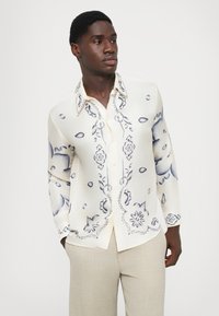 Langärmliges Hemd in Creme mit blauem Blumenmuster, mit einer durchgehenden Knopfleiste und spitzem Kragen, aus glattem, leichtem Stoff gefertigt.