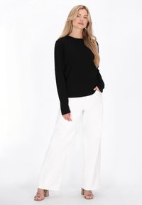 Bluza neagră cu mâneci lungi, cu model în dungi, asortată cu pantaloni albi largi și sandale bej cu toc bloc. Design simplu, fără ornamente vizibile.