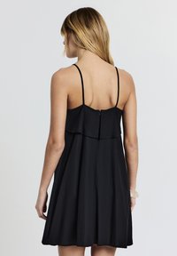 Vestito nero senza maniche con corpetto aderente e design a strati di balze, caratterizzato da una cerniera discreta sul retro e una silhouette fluida.