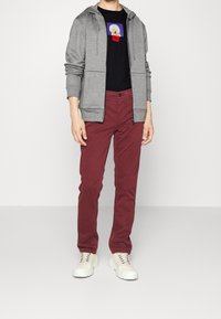 Grå lynlås hoodie over en sort t-shirt med et farverigt grafik, parret med bordeaux bukser og hvide sneakers.