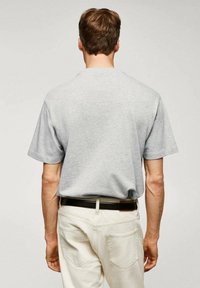 T-shirt grigia a maniche corte, realizzata in morbido cotone, con una vestibilità comoda e scollo rotondo, abbinata a jeans chiari e una cintura nera.