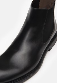 Bottine Chelsea en cuir noir avec une surface lisse, des panneaux latéraux en élastique, un bout arrondi et un petit talon carrée.