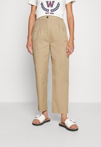 Khaki hoge taille broeken met plooien, gemaakt van een lichtgewicht stof. In combinatie met een wit graphic t-shirt en witte slide sandalen.