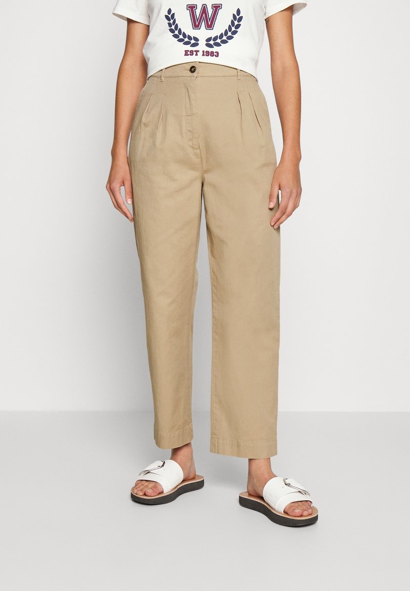 Khaki hoge taille broeken met plooien, gemaakt van een lichtgewicht stof. In combinatie met een wit graphic t-shirt en witte slide sandalen.